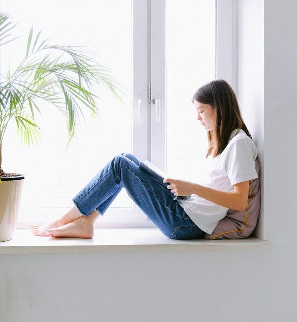 Teenager meditating by a window with soft light coming in.